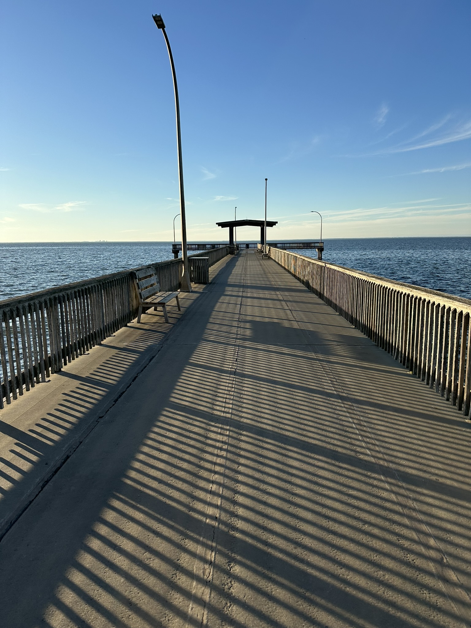 Long waterfront fishing pier casting geometric shadows across its walkway on the Alabama Gulf Coast.