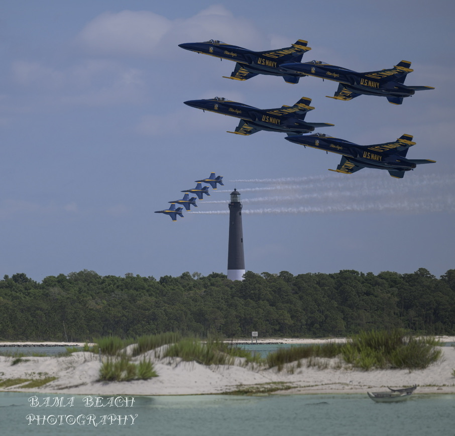 United States Navy Blue Angels flying in formation above a Gulf Coast lighthouse and shoreline.