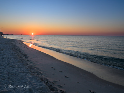 Sunrise casting a long golden reflection along a quiet Gulf Shores beach shoreline.