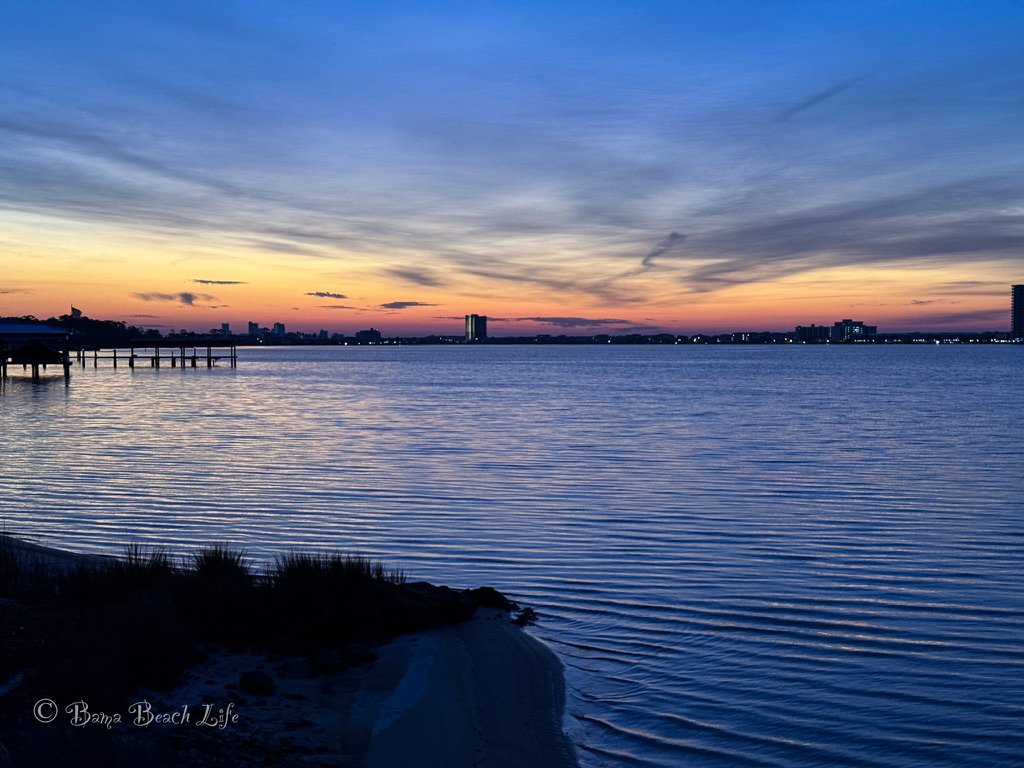 Blue-hour sky and calm Little Lagoon water with the Gulf Shores skyline on the horizon.