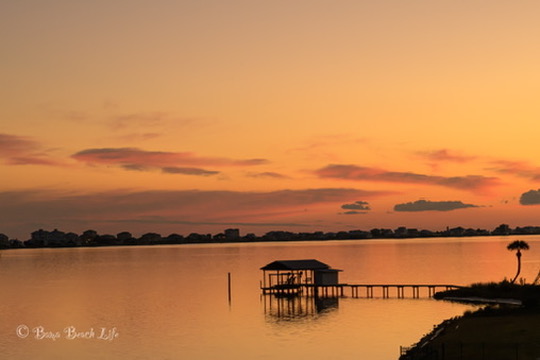 Golden sky, covered boathouse, and tranquil water at Little Lagoon on the Alabama Gulf Coast.
