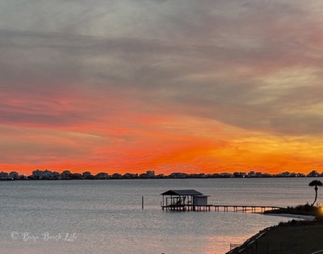 Small covered boathouse and dock silhouetted beneath a vivid Little Lagoon sunset.