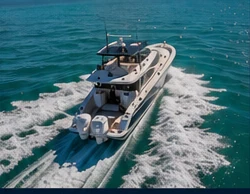 Luxury yacht underway from chase-boat perspective on clear blue and emerald water.